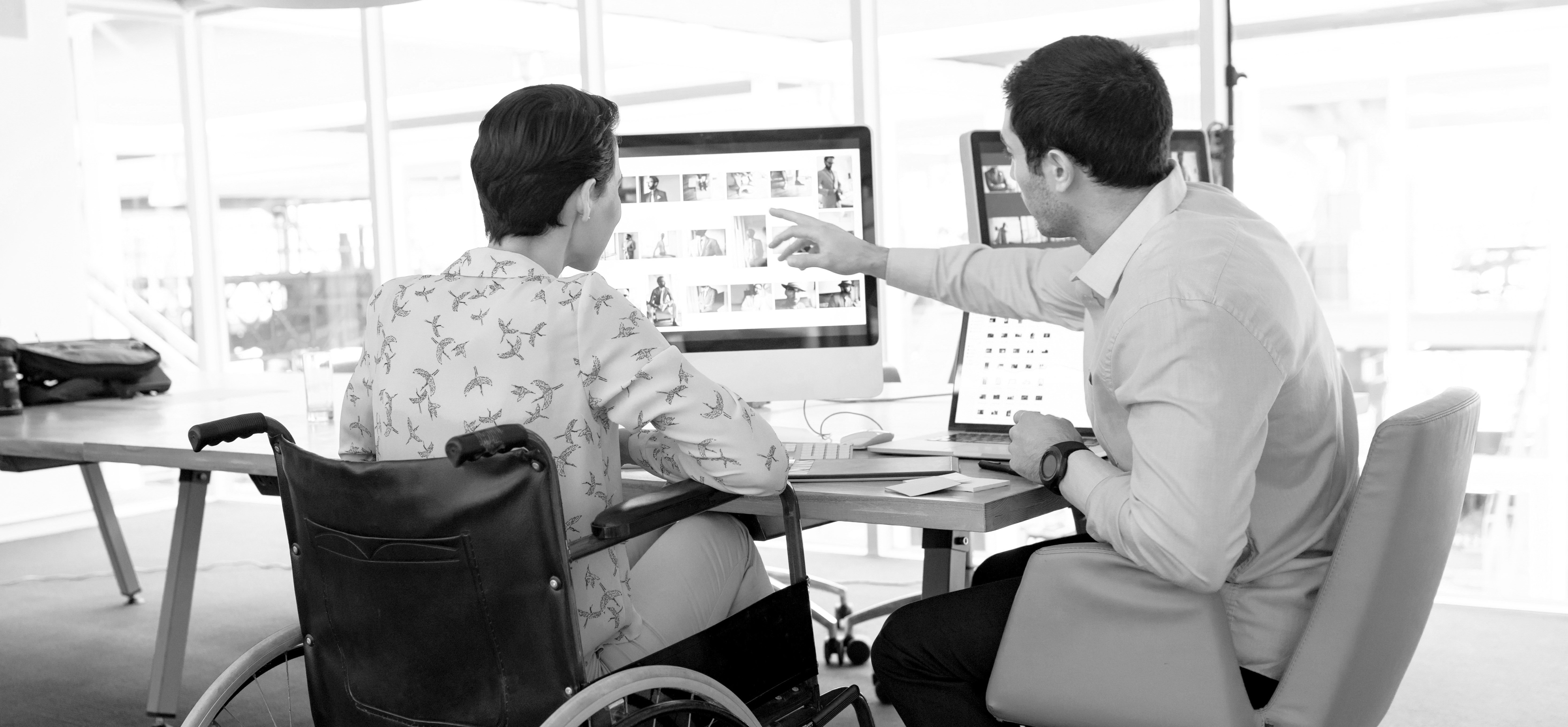 Mann erklärt Frau im Rollstuhl etwas an einem Computer